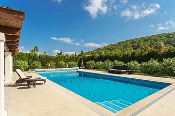 A large swimming pool is surrounded by chairs and trees