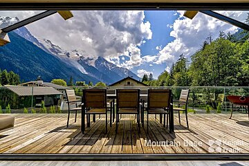 A table and chairs on a deck with mountains in the background