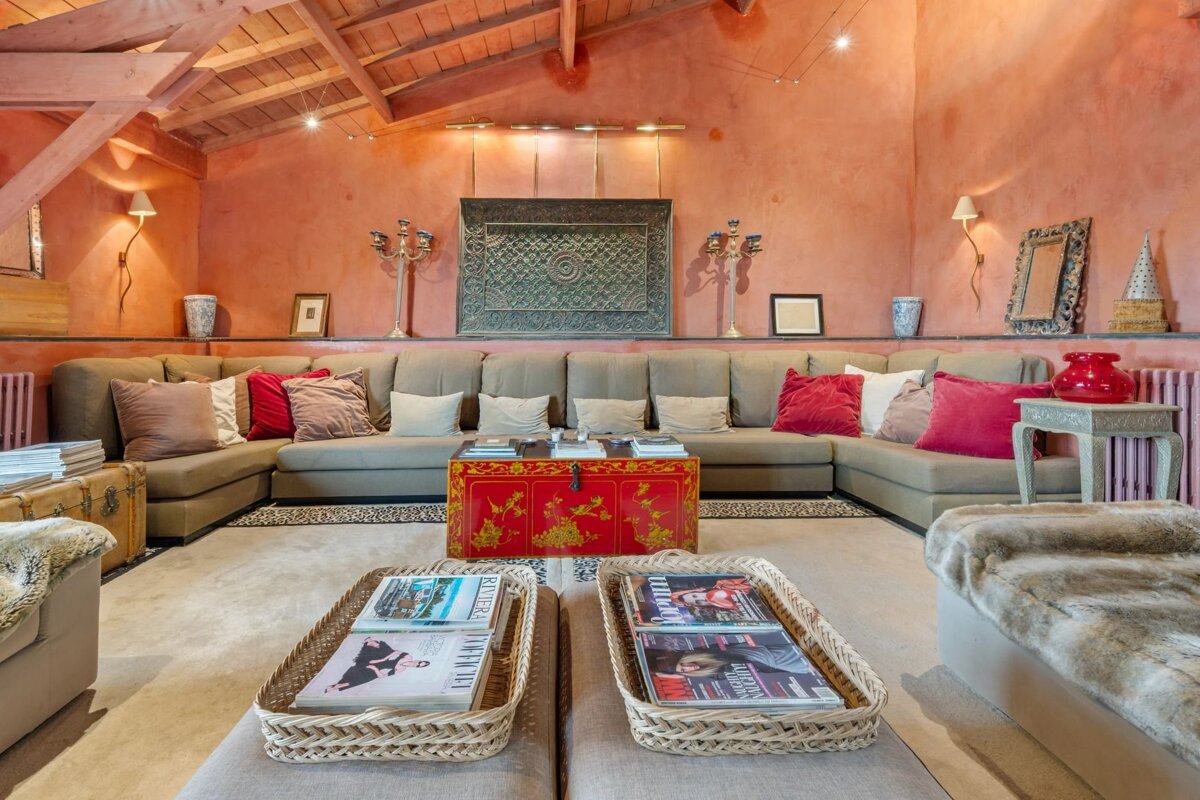 A rustic-chic living room with salmon walls, exposed beams, a huge sectional sofa, a red oriental chest, and woven magazine baskets.