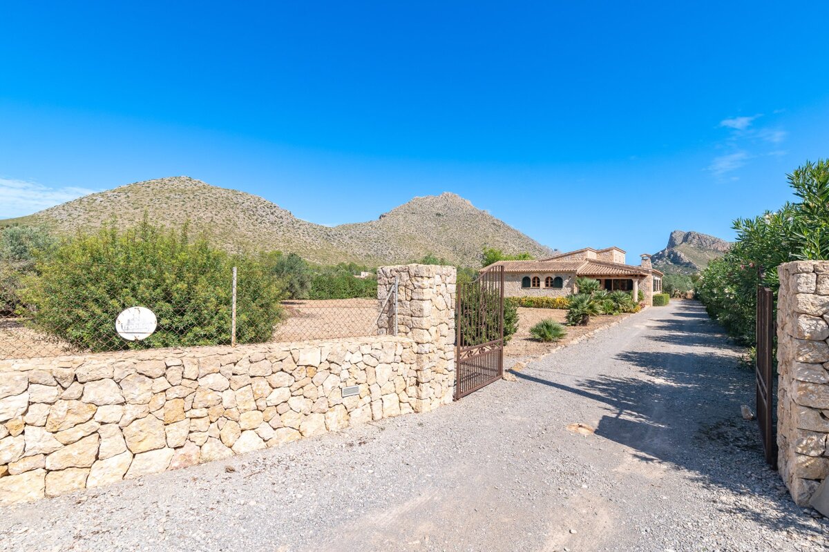 A stone wall surrounds a driveway leading to a house