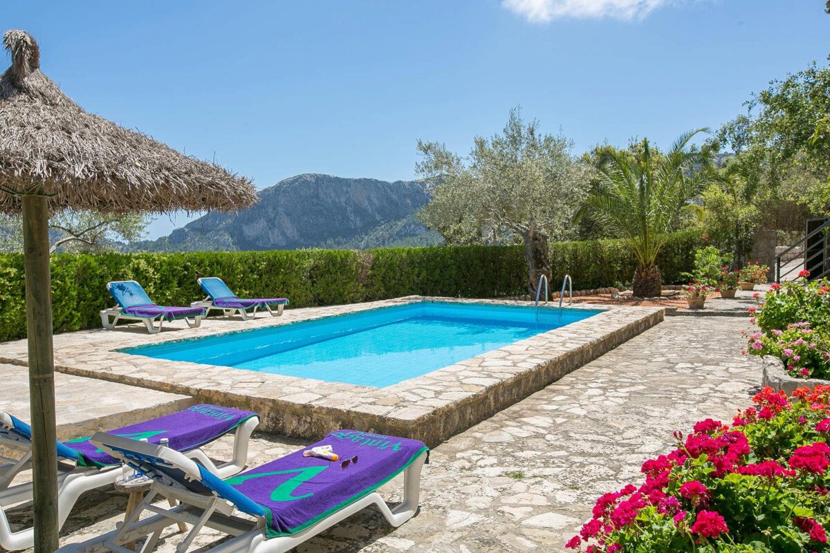 A swimming pool surrounded by chairs and umbrellas with a mountain in the background