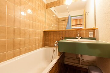 A cozy bedroom features a bed with light bedding nestled into a light wood built-in headboard and storage unit, softly lit, beside a radiator.