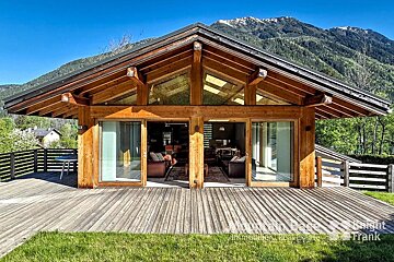 A wooden house with mountains in the background is for sale