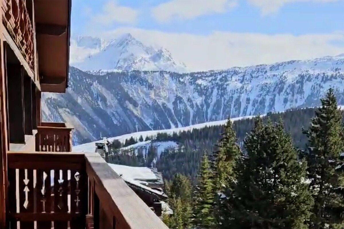 A balcony overlooking a snowy mountain range with trees in the foreground