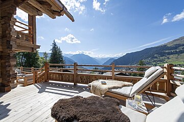 A deck with chairs and a book on it with mountains in the background