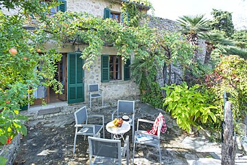 A patio with a table and chairs in front of a stone building with green shutters