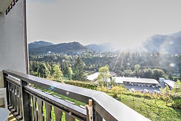 Balcony view of a sunlit mountain valley with a town nestled among trees, bathed in bright sun rays.