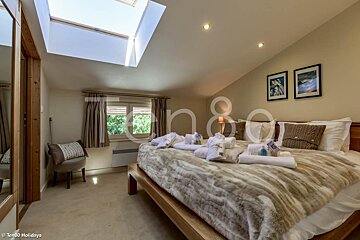 A bedroom with a skylight and a bed with a fur blanket