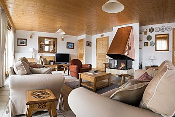 A spacious, cozy living room with a large copper fireplace, comfortable light-colored sofas, a TV, and a prominent wood-paneled ceiling.