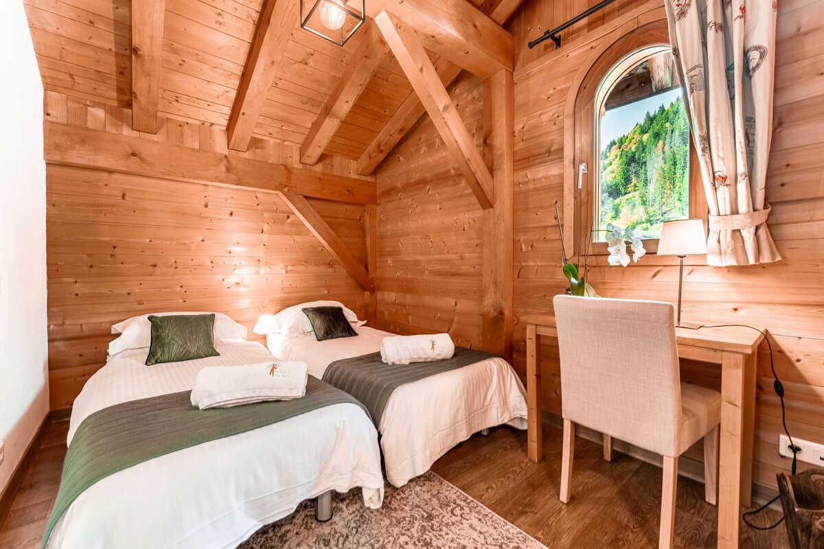 A wooden bedroom with two beds and a desk