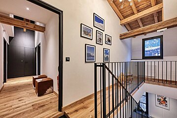 A stylish, spacious interior with light wooden floors, exposed ceiling beams, a black metal staircase, a gallery wall, and a hallway with cowhide stools.