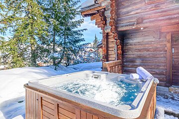 A hot tub in the snow outside of a log cabin