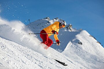 A person wearing a yellow jacket and red pants is skiing down a snowy hill