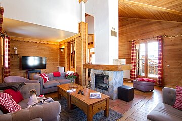 A cozy, wood-paneled living room featuring a stone fireplace, gray sofas with red accents, and a large TV, creating a warm cabin ambiance.