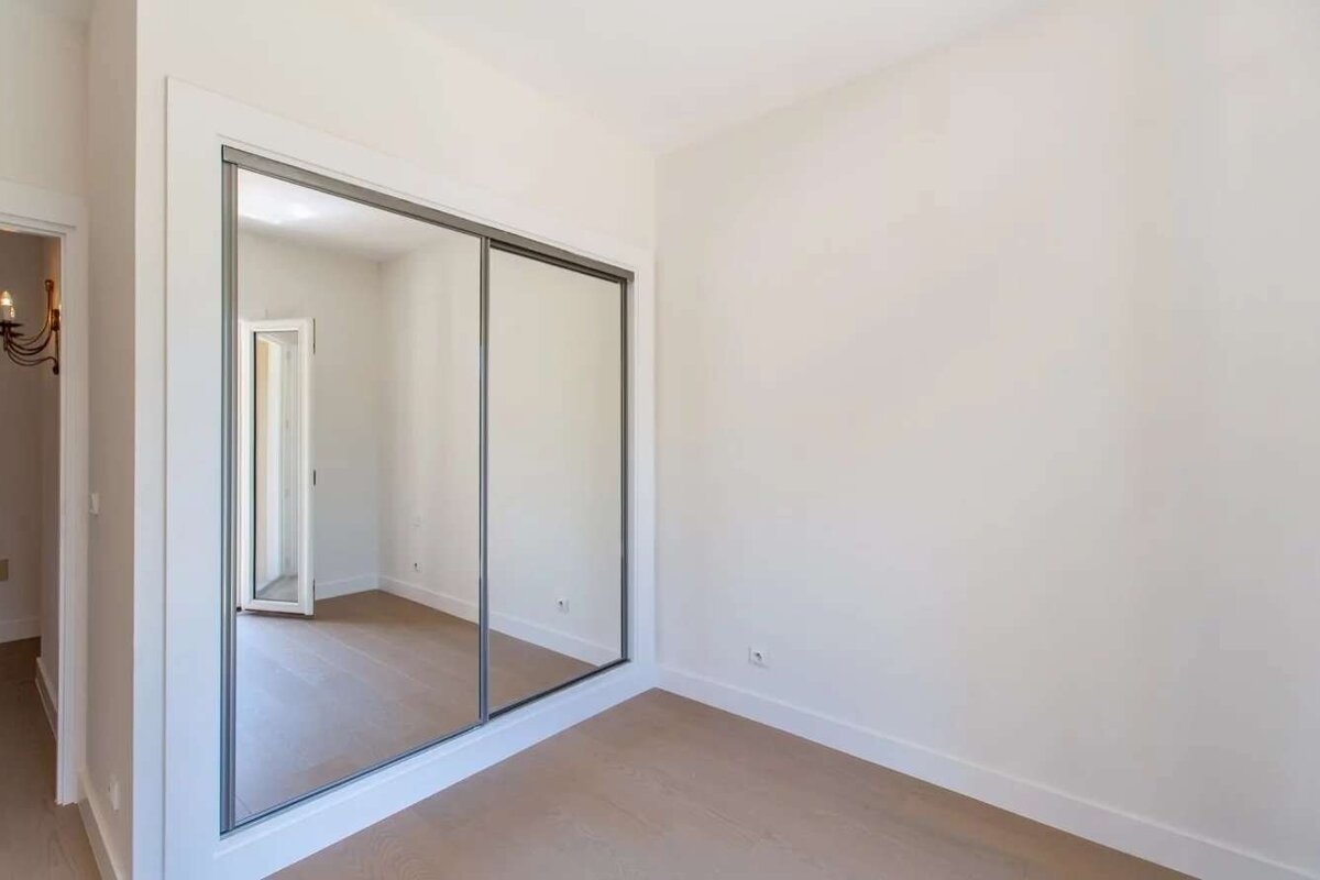 Empty room with white walls, light wood floor, and a large mirrored closet reflecting a doorway. Clean, modern, and unfurnished.