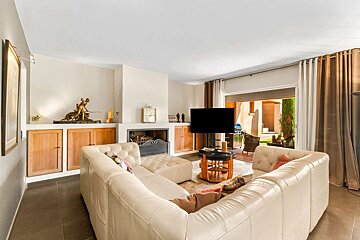 A comfortable living room with a cream sectional sofa, fireplace, TV, wood built-ins, and a view to a sunny patio through sliding glass doors.