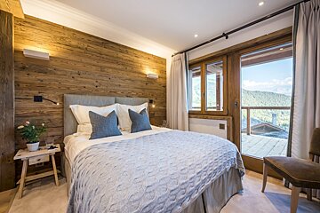A bedroom with a bed and a window with mountains in the background