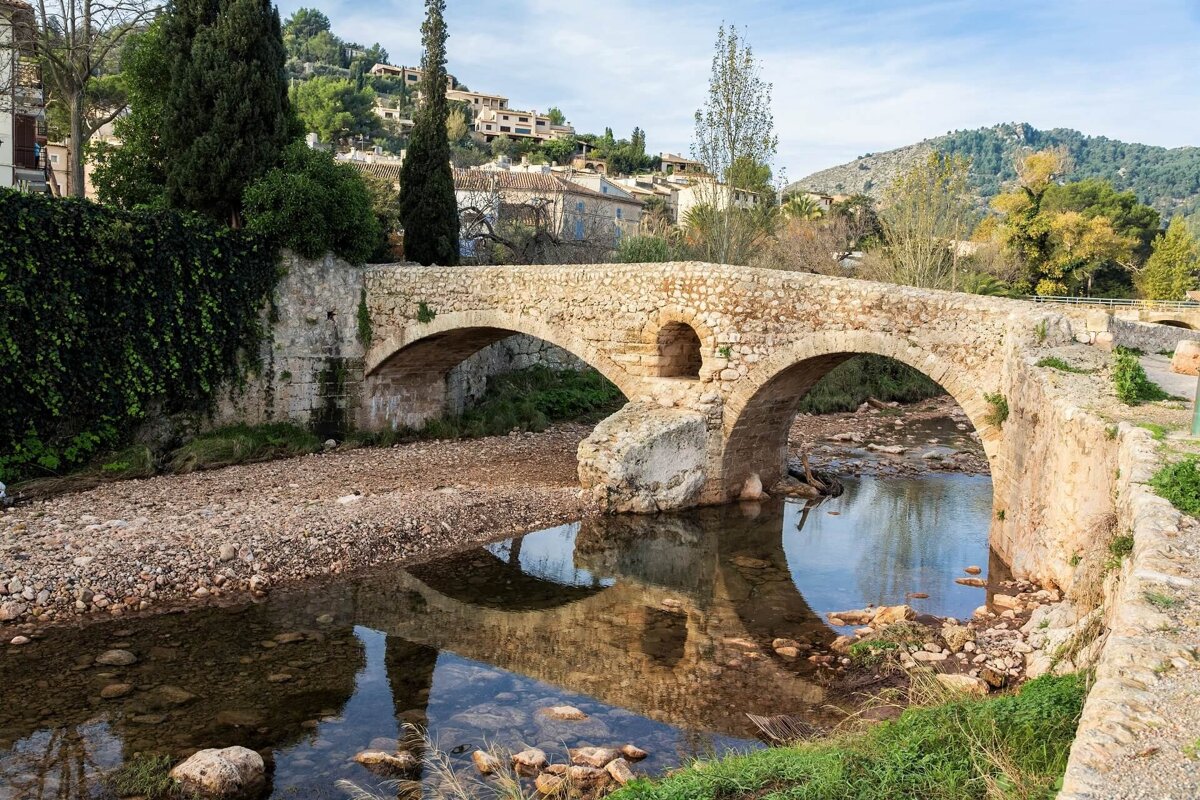 A stone bridge over a river with houses in the background