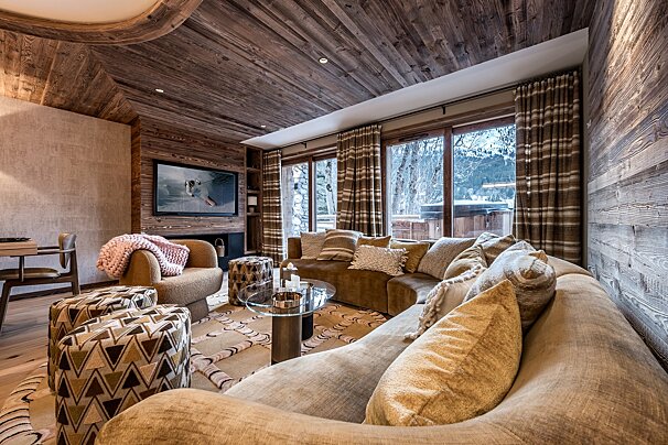 A luxurious, wood-paneled ski chalet living room with comfy sofas, a modern TV, and large windows showcasing a snowy mountain view.