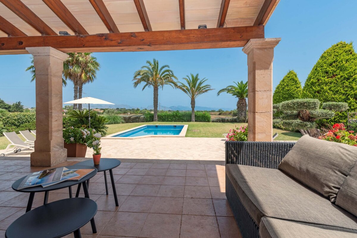 A patio with a couch and tables looking out to a pool