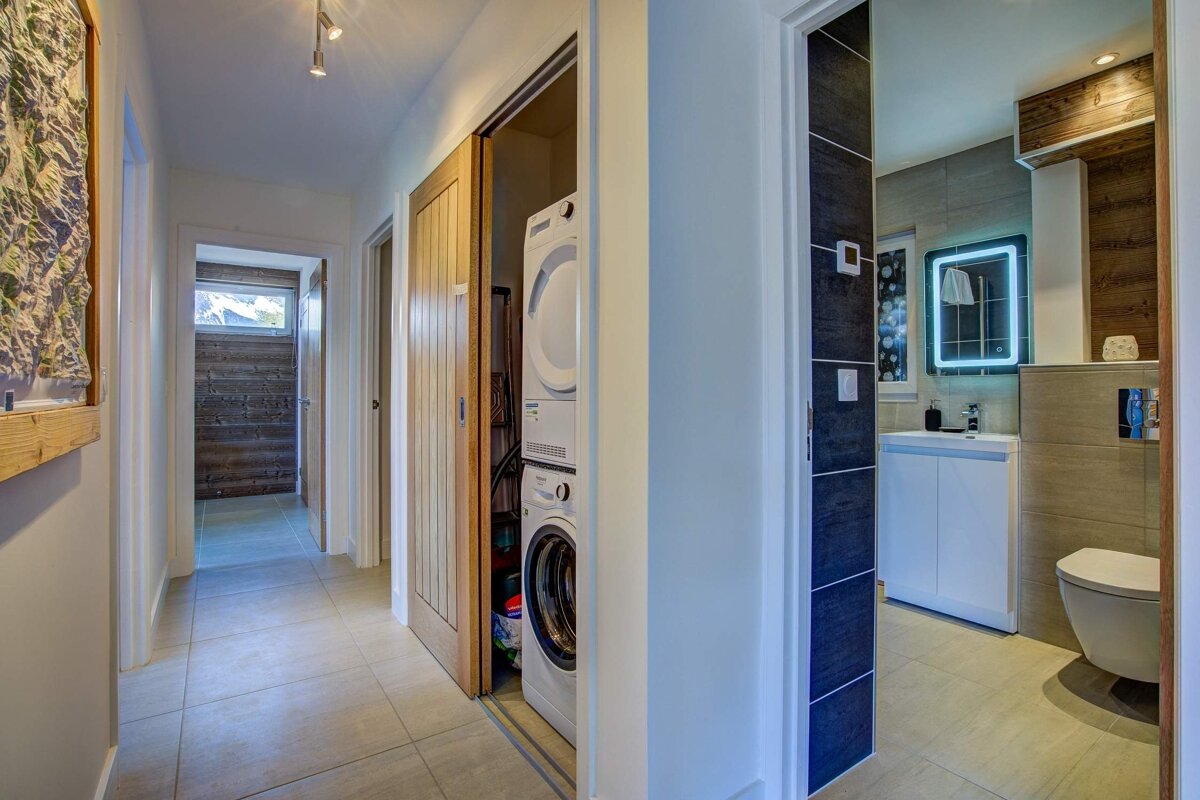 Bright hallway with a closet holding a stacked washer and dryer, next to a modern bathroom with an illuminated mirror.
