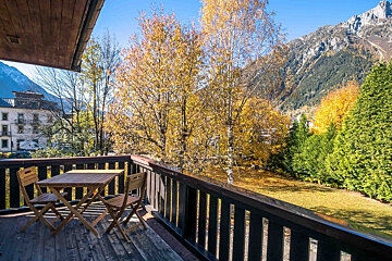 A balcony with a table and chairs and mountains in the background
