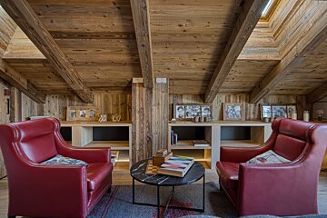 Two red leather armchairs face each other in a cozy, wood-paneled attic room with exposed ceiling beams and a small coffee table.