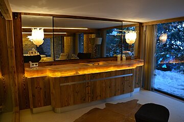 Luxurious wooden spa bathroom with an illuminated counter, large mirror reflecting the interior, and a window overlooking a snowy landscape.