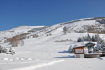 Snowy mountain slopes under a clear blue sky with a ski lift station in the foreground.