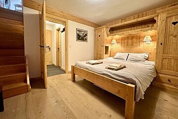 Cozy chalet bedroom featuring all-wooden furniture, a large bed with built-in cabinets, light floors, and stairs on the left.