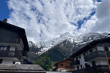 Snow-capped mountains tower behind alpine chalets with dark balconies and roofs under a cloudy sky.