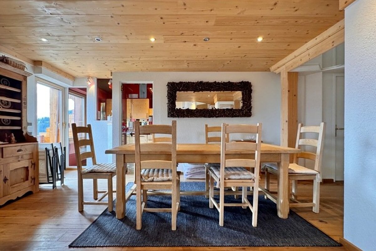 Rustic alpine dining room featuring a wooden table and chairs on a blue rug, set under a warm wood-paneled ceiling.