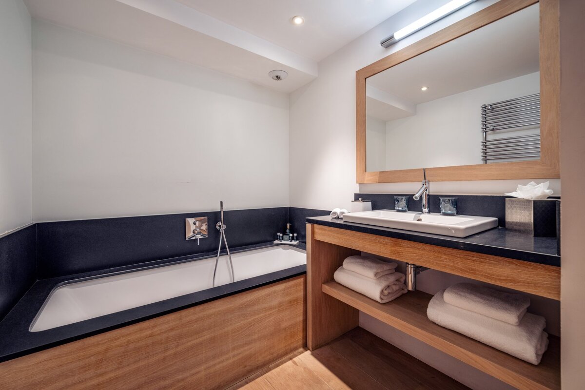 Modern bathroom with a wood-paneled bathtub, a wooden vanity with folded towels, and a large framed mirror.