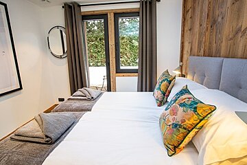 A cozy bedroom with a wooden accent wall, white beds topped with colorful floral pillows, and glass doors to a balcony.
