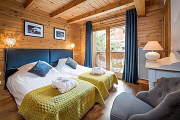 A wooden bedroom with two beds and a chair