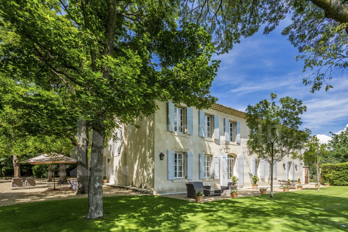 A large white house with blue shutters is surrounded by trees