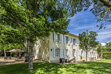 A large white house with blue shutters is surrounded by trees