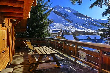 A wooden deck with a picnic table and chairs with a mountain in the background