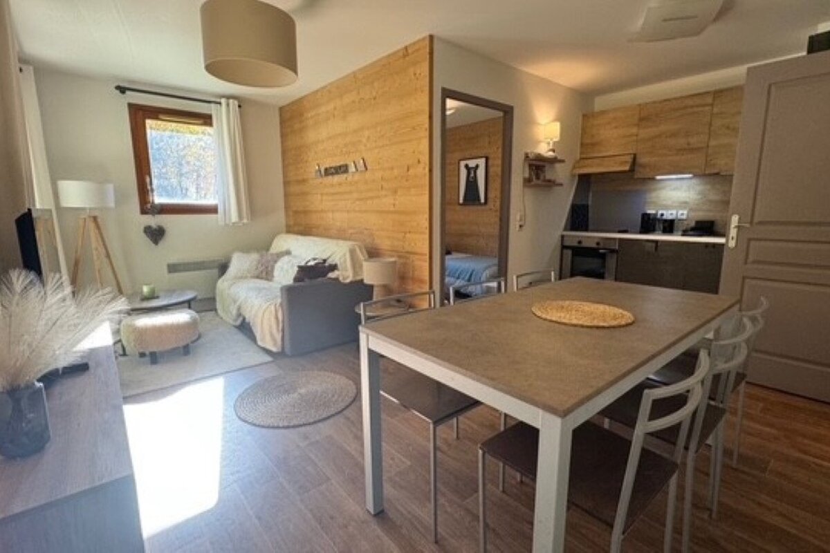 A modern, open-concept studio apartment with a dining area, kitchen, and living room, featuring light wood accents and flooring.