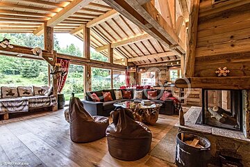 Rustic wooden chalet living room with high beamed ceilings, large windows, a sectional sofa, bean bag chairs, and a fireplace.