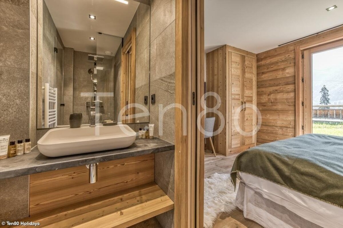 Cozy alpine chalet interior showing a modern stone bathroom alongside a rustic bedroom with warm wooden walls.