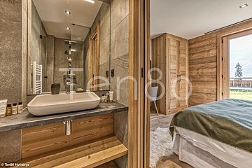 Cozy alpine chalet interior showing a modern stone bathroom alongside a rustic bedroom with warm wooden walls.
