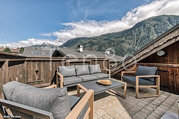 A patio with a couch and chairs with mountains in the background