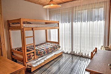 A cozy room featuring a wooden bunk bed with a trundle, sheer white curtains, tiled flooring, and a woven pendant light.