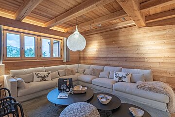 Cozy chalet living room with all-wood walls, a large beige sectional sofa, rustic deer pillows, and a spherical pendant lamp.