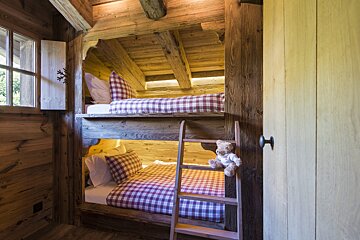 A teddy bear sits on a ladder next to a bunk bed