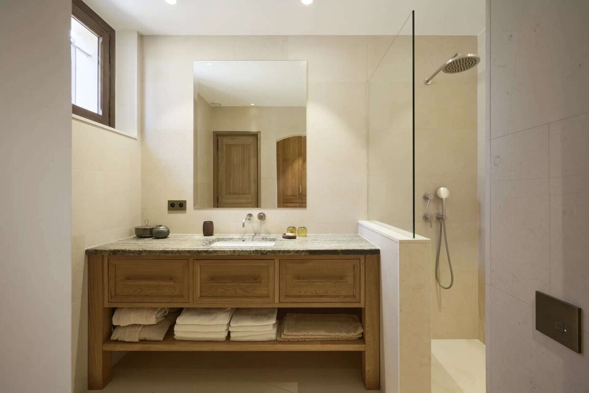 A clean, modern bathroom with a wooden vanity, stone counter, and a large mirror. It includes a walk-in shower with a glass partition and is decorated in neutral tones.