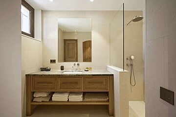 A clean, modern bathroom with a wooden vanity, stone counter, and a large mirror. It includes a walk-in shower with a glass partition and is decorated in neutral tones.