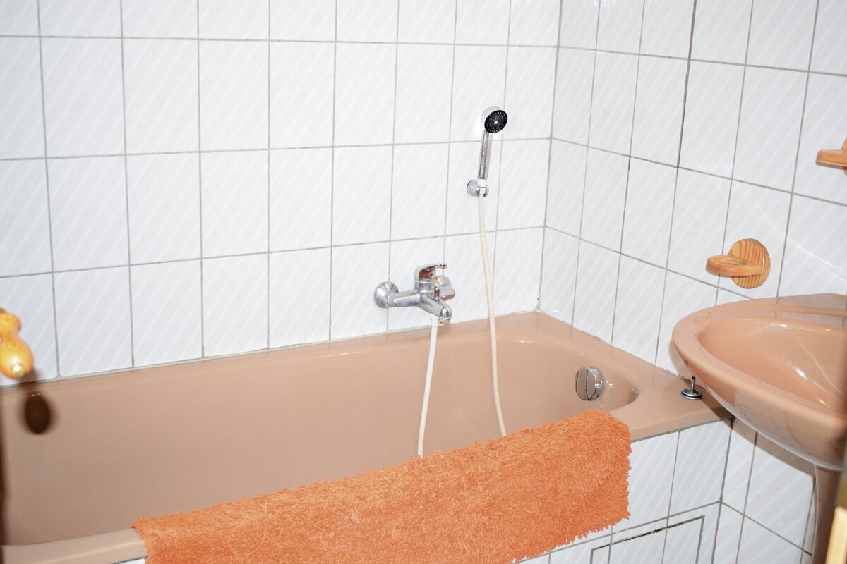 Peach-colored bathtub and sink with white tiled walls, featuring an orange towel draped over the tub edge.