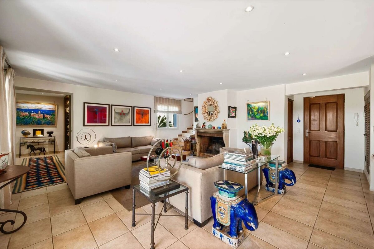 A bright, inviting living room featuring tan sofas, an array of colorful artwork, a rustic fireplace, and unique decorative accents.